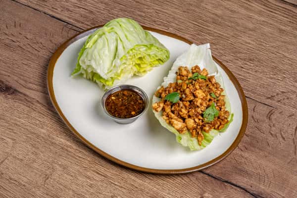 Minced chicken lettuce wrap topped with cilantro, served with a side of soy-based dipping sauce on a white plate.