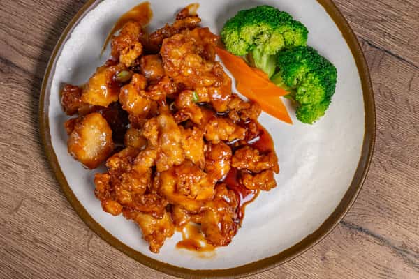 Orange chicken glazed in sweet and tangy sauce, served with steamed broccoli and sliced carrots on a white plate.