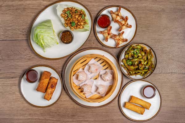 Assorted Chinese dishes including dumplings, noodles, fried rice, and stir-fried vegetables served on a wooden table.