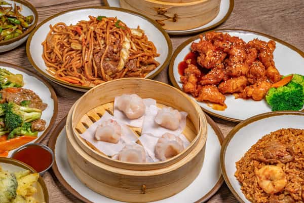 Assorted Chinese dishes including dumplings, noodles, fried rice, and stir-fried vegetables served on a wooden table.