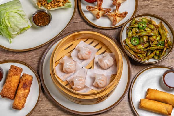 Assorted Chinese dishes including dumplings, noodles, fried rice, and stir-fried vegetables served on a wooden table.