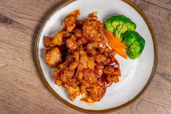 Orange chicken glazed in sweet and tangy sauce, served with steamed broccoli and sliced carrots on a white plate.