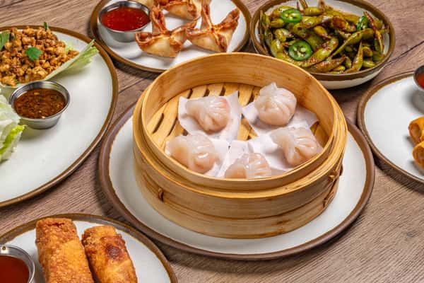 Assorted Chinese dishes including dumplings, noodles, fried rice, and stir-fried vegetables served on a wooden table.