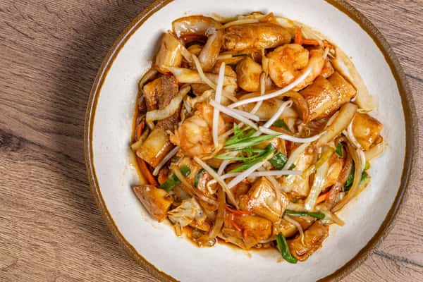 Stir-fried flat rice noodles with shrimp, tofu, bean sprouts, cabbage, and scallions in a savory brown sauce.