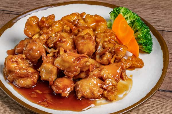 Orange chicken glazed in sweet and tangy sauce, served with steamed broccoli and sliced carrots on a white plate.