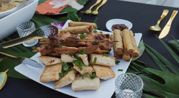 A tray filled with egg rolls and meat skewers