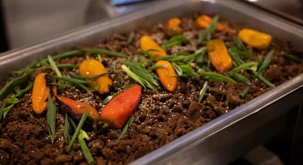 A chafing dish filled with a beef dish garnished with peppers and scallions