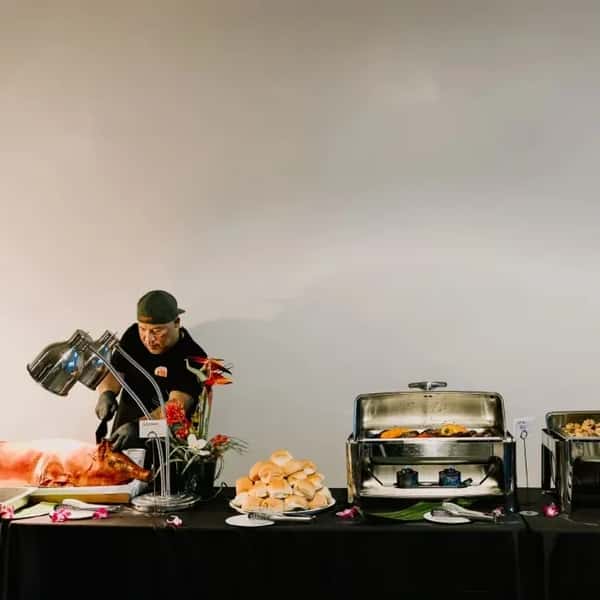 Kalei's staff member standing behind a table with catered food and chafing dishes for an event