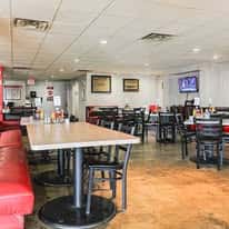 Casual dining restaurant interior with red booths, black chairs, wooden tables, and a TV mounted on the white wall.