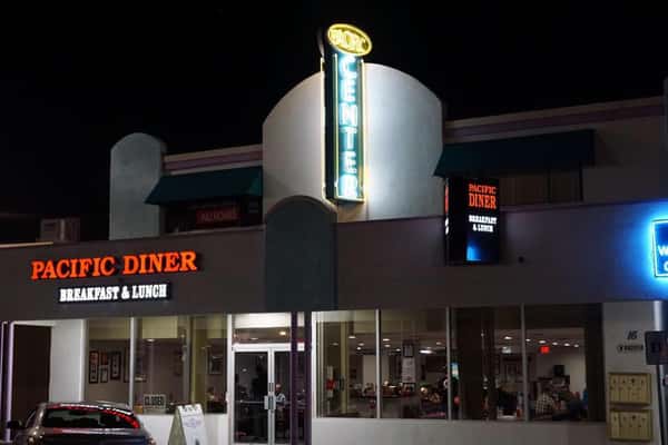 Pacific Diner at night with glowing neon signs and a view of customers dining inside.