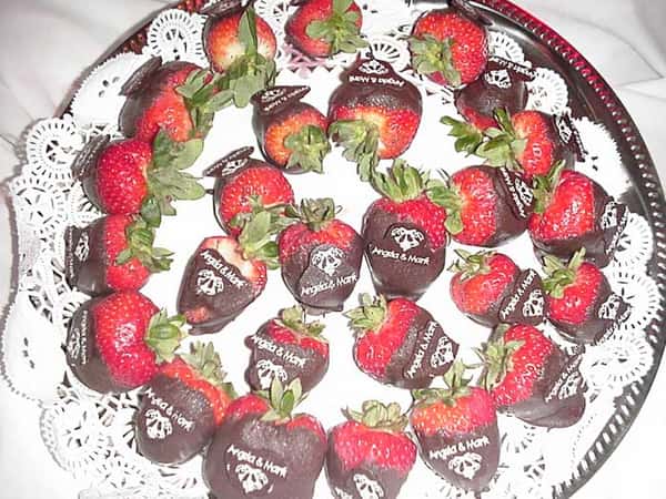 several chocolate-covered strawberries on a dish, with "Angela & Mark" written on each one in white chocolate