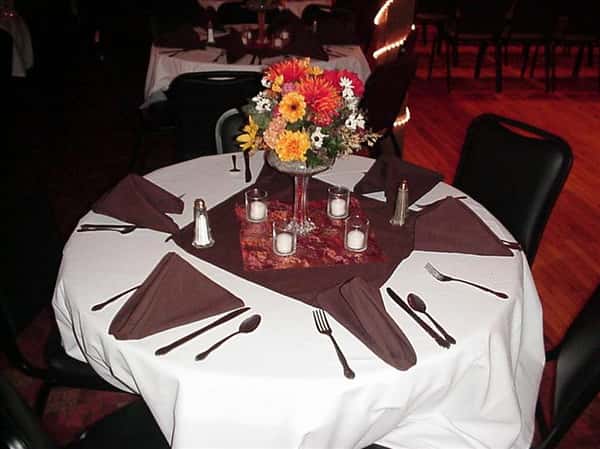 table set with folded napkins, eating utensils, and a flower vase centerpiece