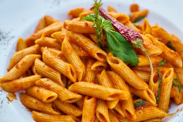 Penne pasta in a spicy tomato sauce garnished with fresh basil and a dried red chili pepper.