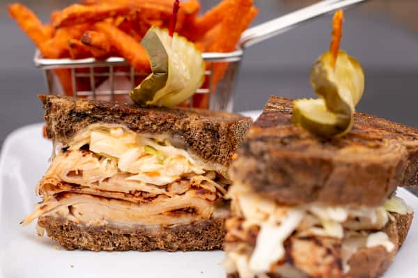 Grilled turkey sandwich on dark rye with melted cheese and pickles, served with sweet potato fries.