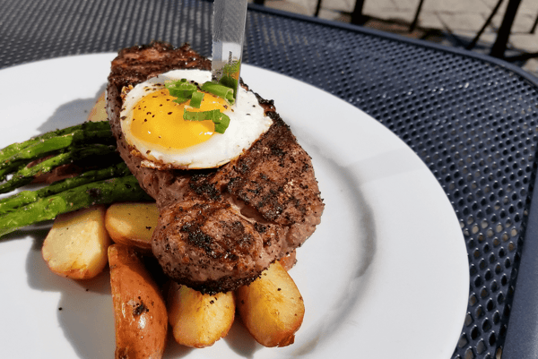 Grilled steak topped with a sunny-side-up egg and green onions, served with roasted potatoes and asparagus.
