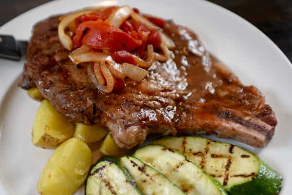 Grilled steak topped with sautéed onions and red peppers, served with roasted potatoes and grilled zucchini.