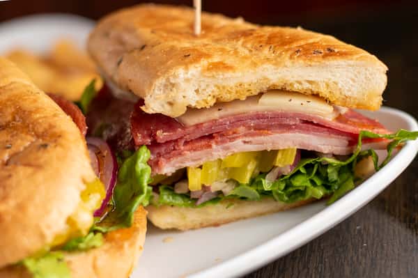 Toasted sub sandwich stacked with ham, salami, and turkey, topped with cheese, lettuce, red onion, and peppers.