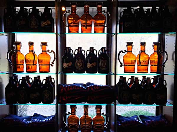 Backlit shelves displaying amber glass growlers and Rivals-branded merchandise against a window backdrop.