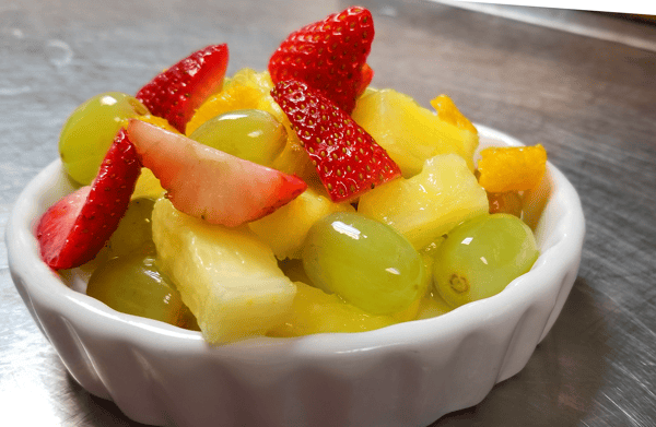 Fresh fruit bowl with strawberries, green grapes, pineapple, and orange segments in light syrup.