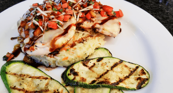 Grilled chicken topped with melted cheese and bruschetta, served over rice with grilled zucchini slices.