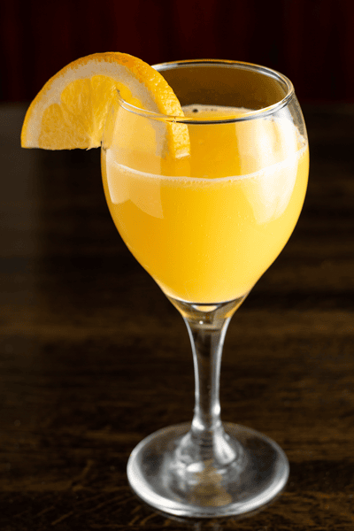 Glass of orange juice garnished with a fresh orange slice on a wooden table background.