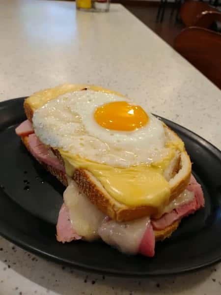 Open-faced Croque Madame sandwich topped with a sunny-side-up egg, layered with sliced ham and melted cheese on thick white bread — a French-inspired brunch favorite with a creamy, savory finish.