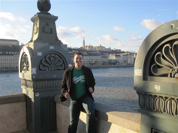 Man wearing Howard's Pub t-shirt sitting on bridge ledge looking over the Danube River in Budapest