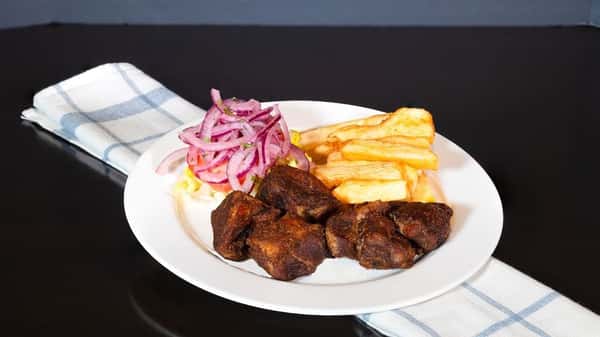 The image shows a plate of *chicharrón* (fried pork), accompanied by fried yuca (cassava), and a fresh red onion salad on a bed of lettuce. This is a traditional Latin American or Caribbean dish, often served with tangy or spicy condiments.