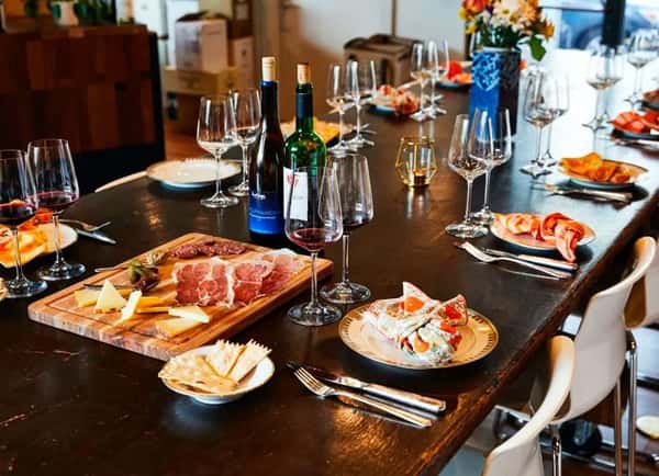 Elegant dining table set with wine glasses, charcuterie board, antipasto, and bottles of red wine, ready for a group meal.