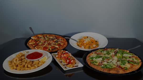 Italian meal spread with two pizzas, a bowl of pasta, bruschetta, and fried calamari served with marinara sauce and lemon wedges.