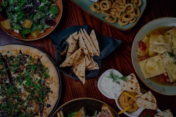 Assorted dishes including flatbread pizza, ravioli, pita bread with dips, fried calamari, and a mixed greens salad.