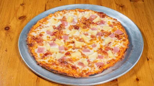 Hawaiian pizza with pineapple chunks, diced ham, and melted mozzarella on a metal tray.