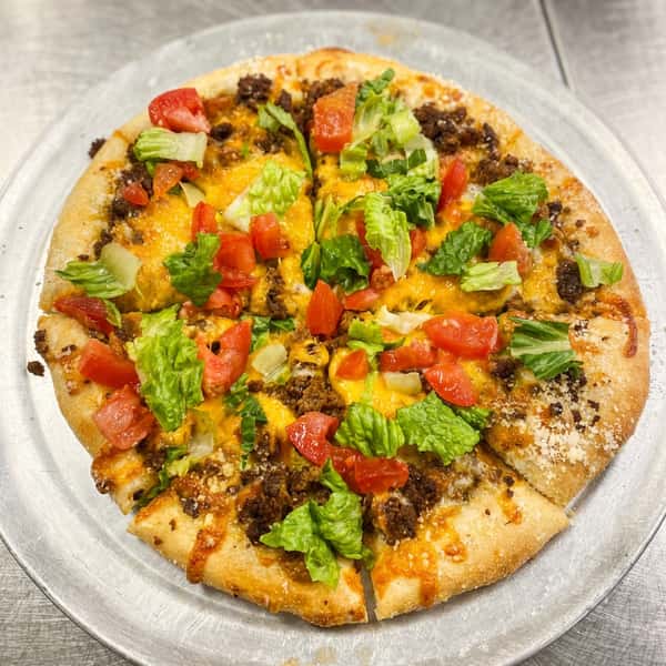Taco pizza with seasoned ground beef, melted cheddar cheese, diced tomatoes, and shredded lettuce on a metal pan.