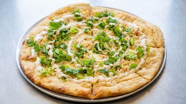 Caesar chicken pizza with white sauce, shredded chicken, and green lettuce, sliced on a metal tray.