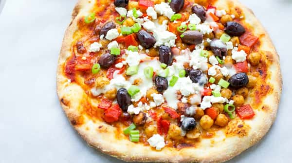 Flatbread pizza topped with red sauce, chickpeas, red bell peppers, black olives, crumbled feta, and chopped green onions.