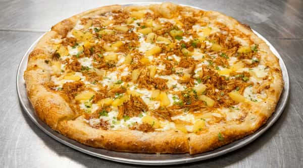 BBQ chicken and pineapple pizza with melted mozzarella and green herbs on a metal pan.