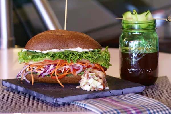 Crisp lettuce, shredded carrots, red cabbage, onions, and tomatoes stacked high on whole wheat bread with a creamy spread — a vibrant, crunchy vegetarian sandwich perfect for clean, plant-based dining.