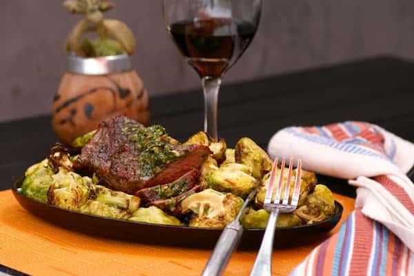 Grilled steak topped with vibrant chimichurri sauce, served over roasted Brussels sprouts — a bold and herbaceous entrée that's perfect for lovers of Latin-inspired steakhouse cuisine.