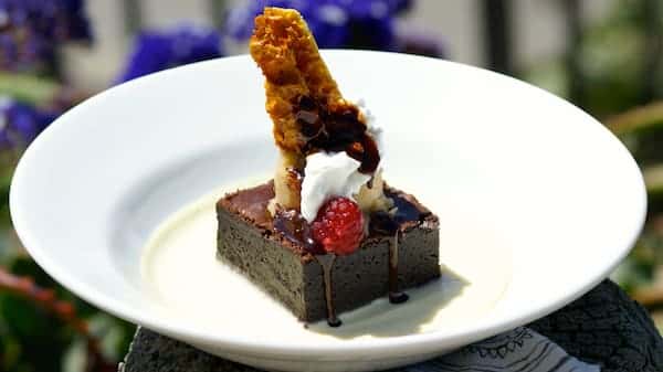 A bold finale of rich dark chocolate cake, drenched in silky crème anglaise and finished with a crisp caramel tuile, fresh raspberry, whipped cream, and a decadent drizzle of chocolate ganache.