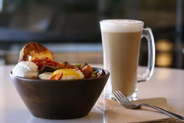 earty farm-style breakfast bowl with eggs, roasted potatoes, sausage, seasonal veggies, and toast — served with a creamy latte for a comforting, protein-packed start to your day.