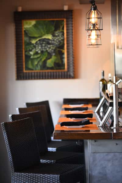 Elegant bar seating with warm lighting and rustic décor, featuring a grapevine painting at Maro Wood Grill.