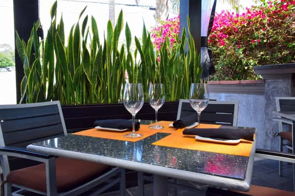 Chic and inviting outdoor patio setup with sleek black chairs, modern place settings, and lush greenery — perfect for relaxed al fresco dining in a stylish, garden-inspired atmosphere.