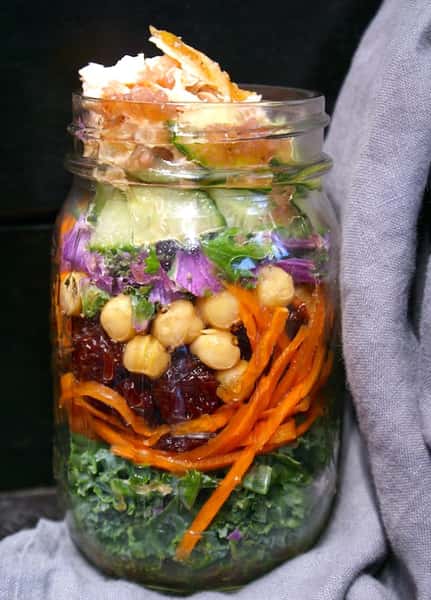 Layered mason jar salad with flaked salmon, kale, chickpeas, carrots, cucumbers, dried cranberries, and creamy goat cheese — a fresh, protein-packed grab-and-go option that's perfect for healthy dining.