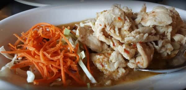 A close-up of a chicken or tofu stir-fry dish served with a side of shredded carrots