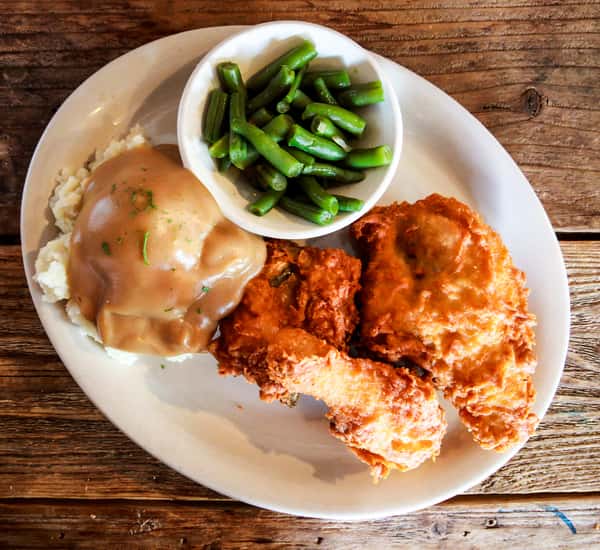 A comforting homestyle dinner featuring crispy fried chicken, creamy mashed potatoes with gravy, and a side of fresh green beans. The plate captures the rich, down-home flavors Judy's Country Kitchen is known for.