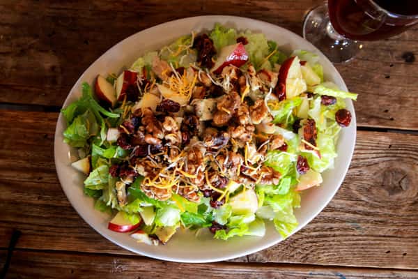 A fresh, hearty salad topped with grilled chicken, shredded cheese, crispy onions, and colorful vegetables. Served in a large bowl, the dish offers a delicious balance of crisp greens and savory country-style flavor.