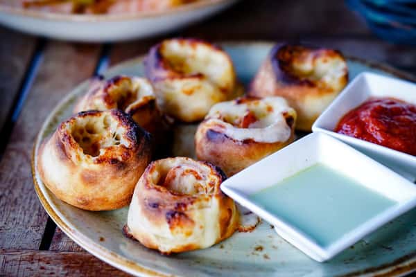 Golden-baked pizza rolls filled with melted cheese and pepperoni, served on a rustic ceramic plate with sides of marinara and creamy garlic dipping sauces.