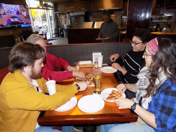 Group of friends sharing pizza slices and drinks at a cozy pizzeria booth