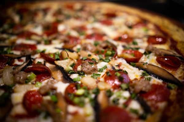close up of supreme pizza with pepperoni, sausage, mushrooms, and fresh herbs