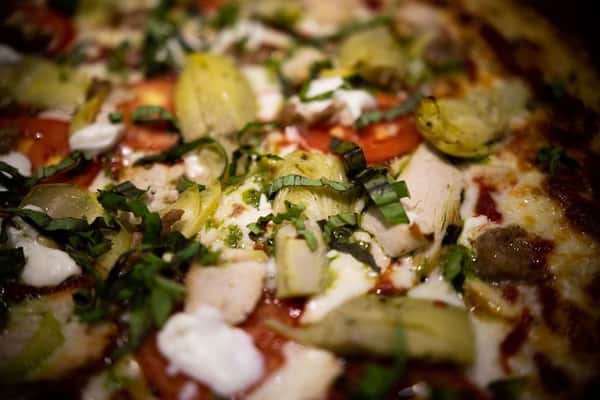 close up of chicken vegetable pizza with artichokes, herbs, and creamy cheese